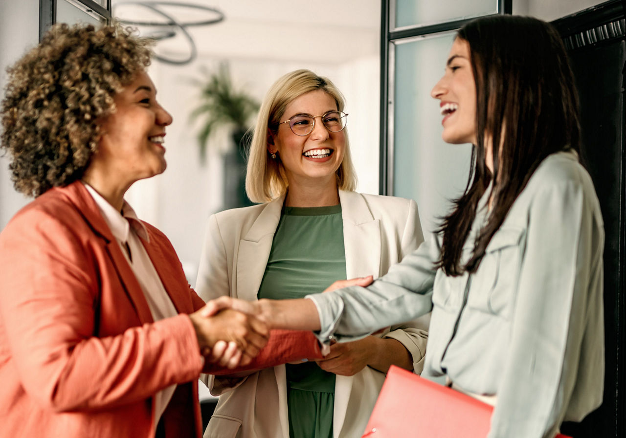 Drei Frauen stehen lächelnd zusammen. 