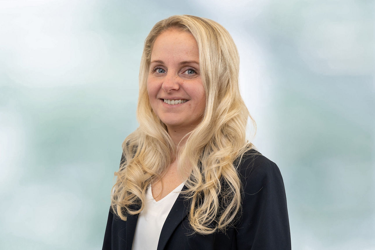 Portrait unserer Mitarbeiterin Christina Fichera. Weiße Bluse, dunkelblaues Jacket, freundlich lächende, blonde Frau.