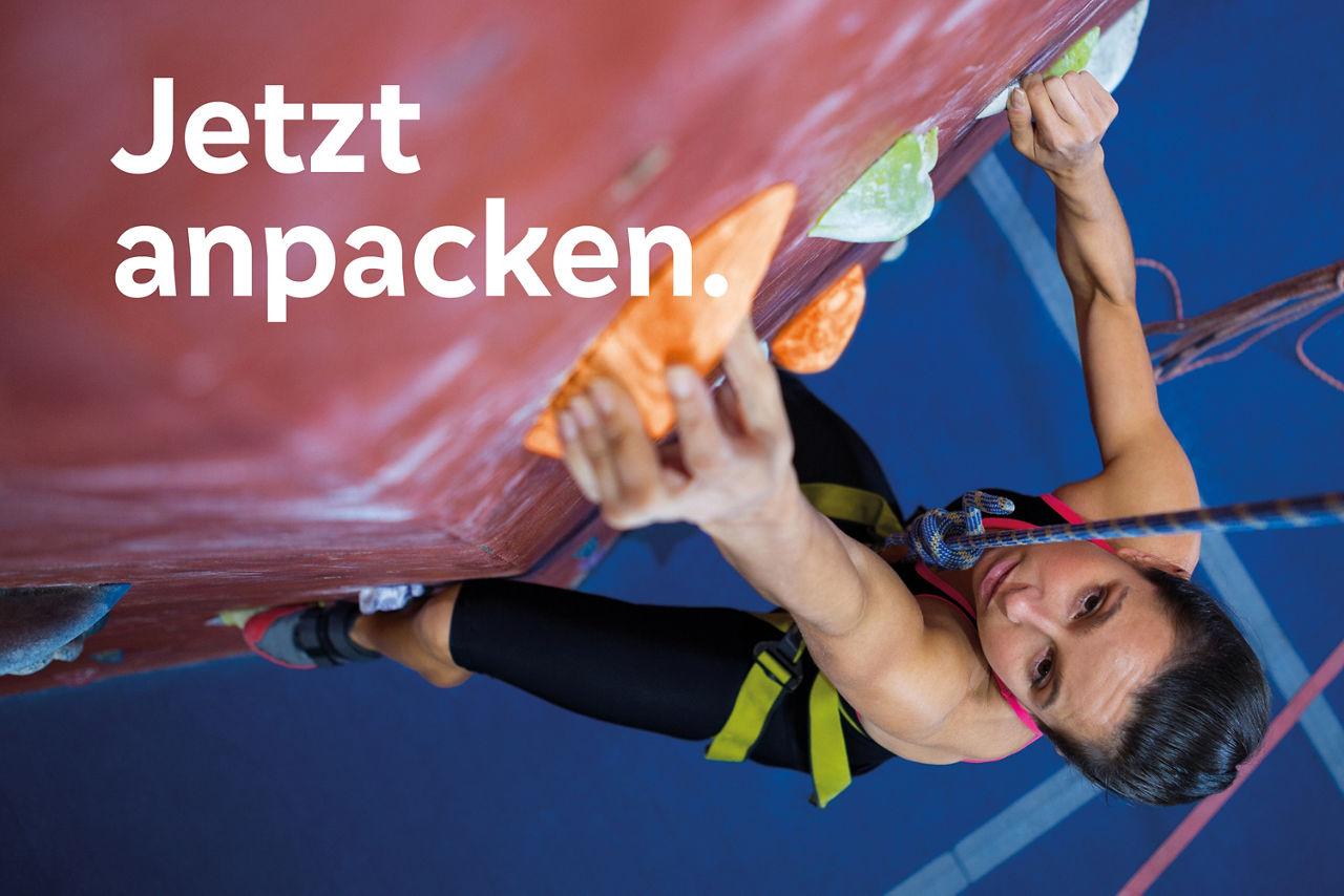 Eine Frau klettert mit Sicherung eine Wand hoch. Text im Bild: Jetzt anpacken. 