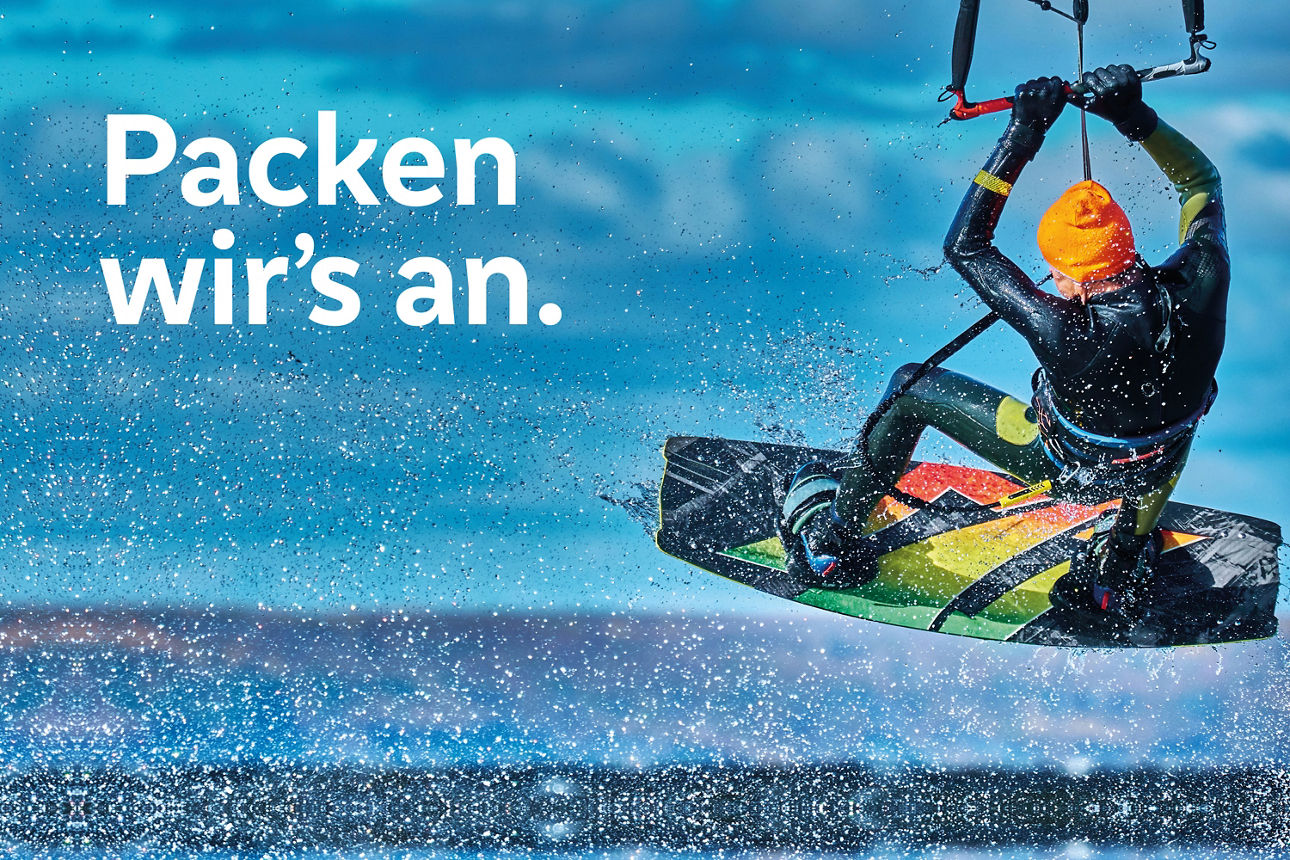 Kitesurfer springt über das Wasser, vor blauem Himmel. Text im Bild: "Packen wir’s an."