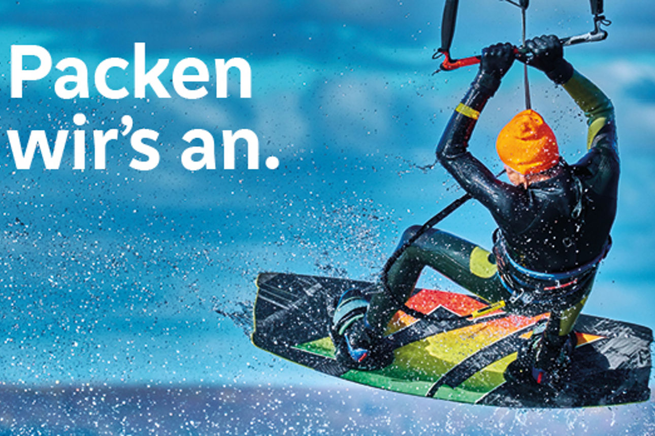 Kitesurfer springt über das Wasser, vor blauem Himmel. Text im Bild: "Packen wir’s an."