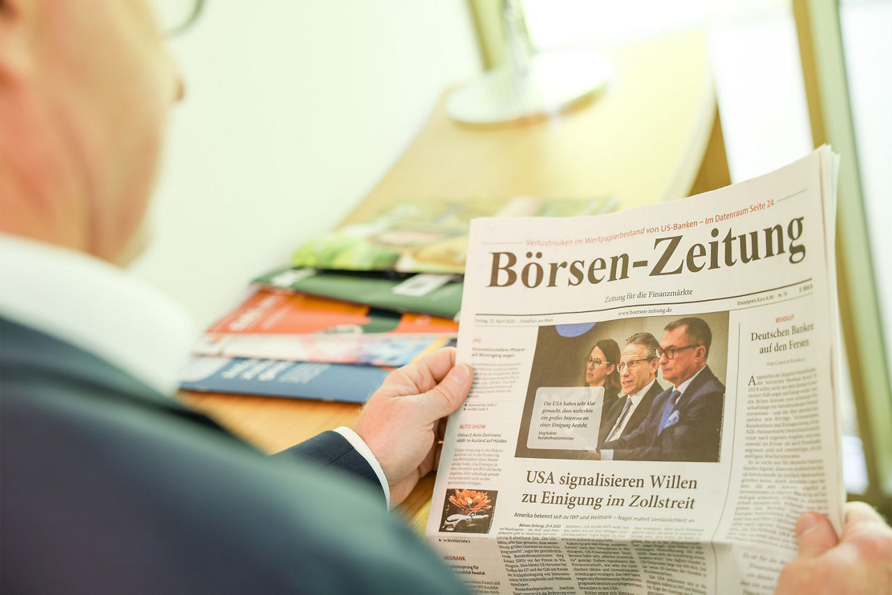 Ein Mann hält eine Zeitung mit der Aufschrift "Börsen-Zeitung" in der Hand und liest diese.