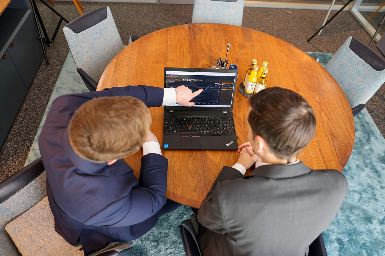 Zwei Berater sitzen an einem Tisch und blicken in einen Laptop auf dem ein Dashboard zu sehen ist