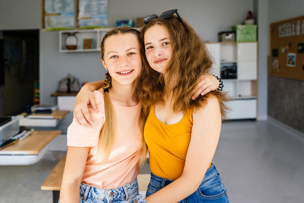 Zwei jugendliche Mädchen Arm in Arm in einem Klassenraum