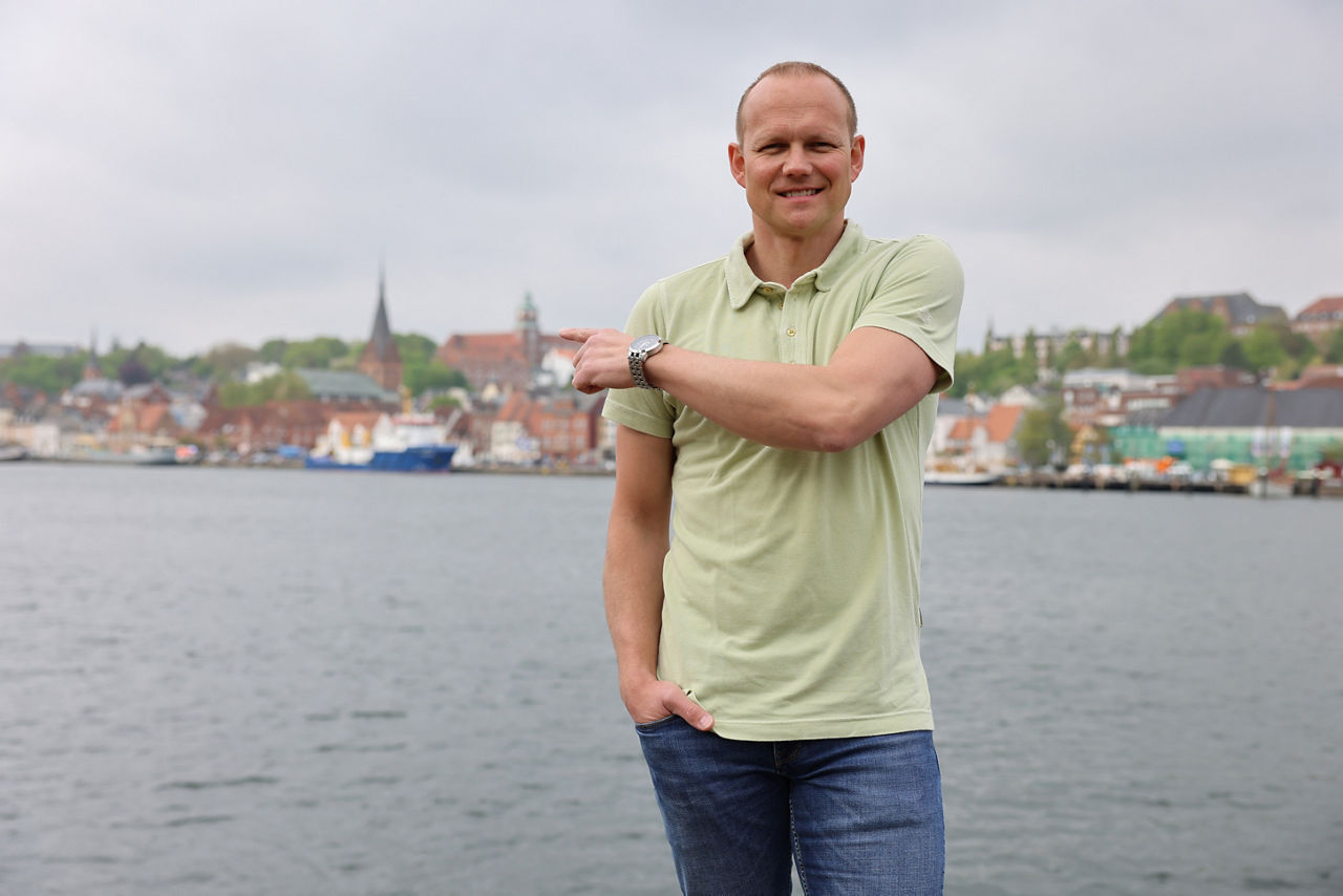 Ein Mann steht vor der Flensburger Förde und zeigt hinter sich