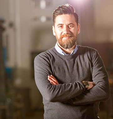 Ein bärtiger Mann in einem Pullover steht in einer Fabrik
