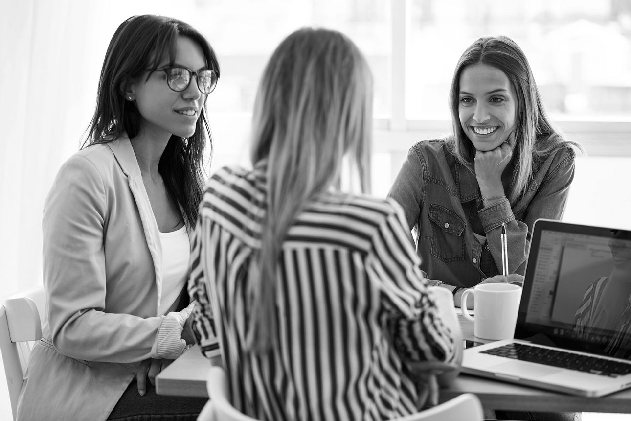 Drei Frauen sitzen am Tisch und sprechen miteinander.