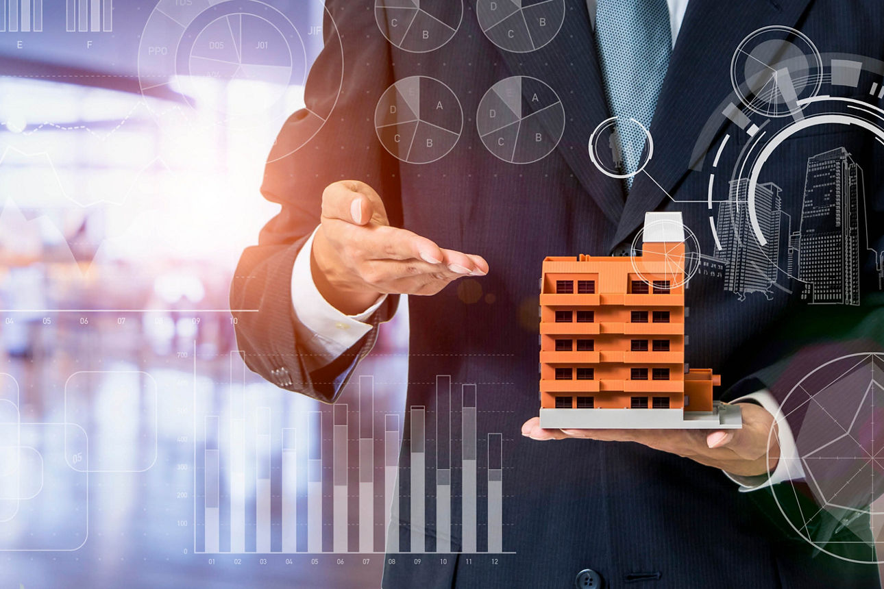 Ein Geschäftsmann im Anzug steht mit ausgestreckten Händen da und hält ein kleines Modell eines Gebäudes