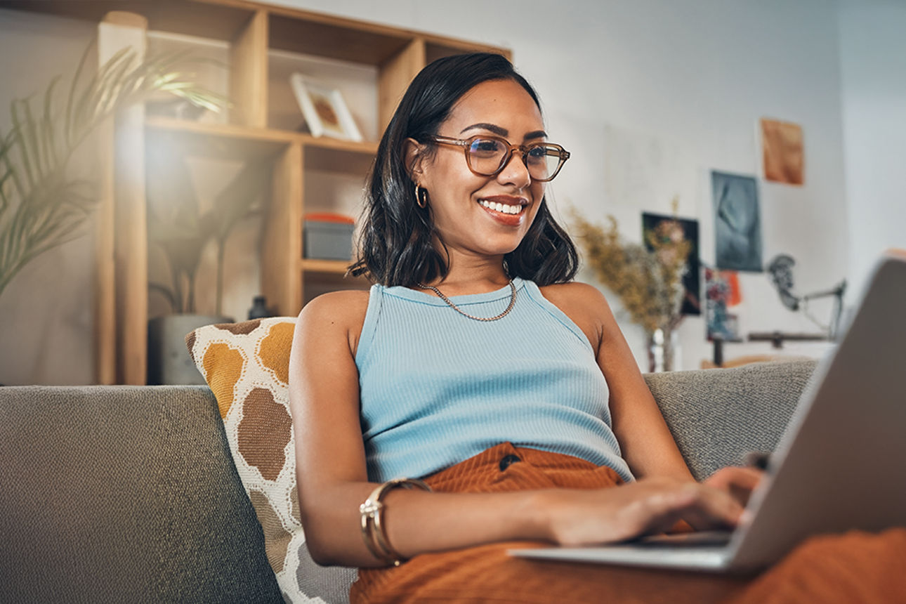 Frau sitzt mit dem Laptop auf den Beinen auf dem Sofa zuhause