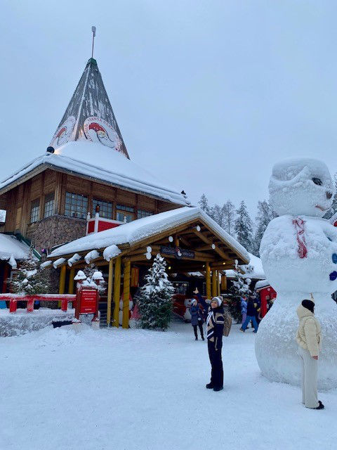 im Vordergrund ein riesiger Schneemann doppelt so hoch wie ein Mensch und im Hintergrund das Haus des Weihnachtsmanns