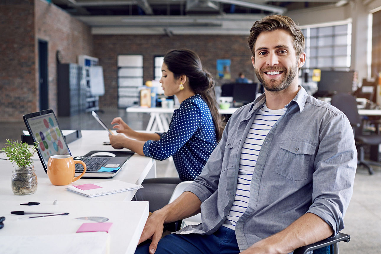 Junger Mann sitzt lachend mit einer Frau im Büro