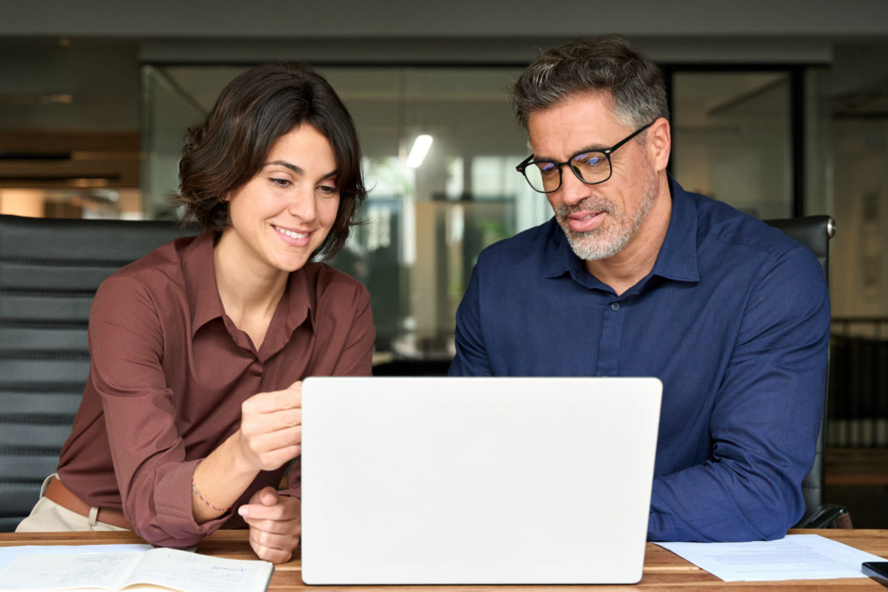 Ein Mann und eine Frau sitzen im Büro und schauen auf ein Laptop. 