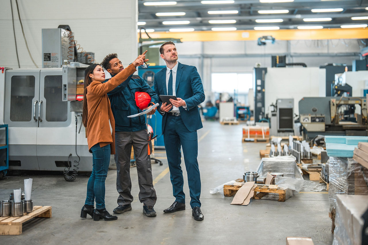 In einer Produktionshalle erklärt eine Produktionsleiterin zwei Besuchern den Produktionsablauf In einer Produktionshalle erklärt eine Produktionsleiterin zwei Besuchern den Produktionsablauf