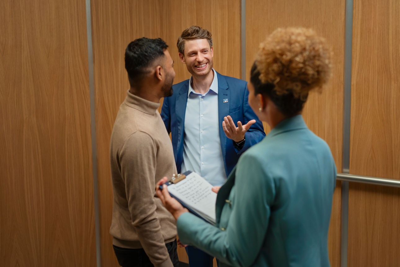 Ein Mann der einen anderen Mann und eine Frau in einem Aufzug berät.