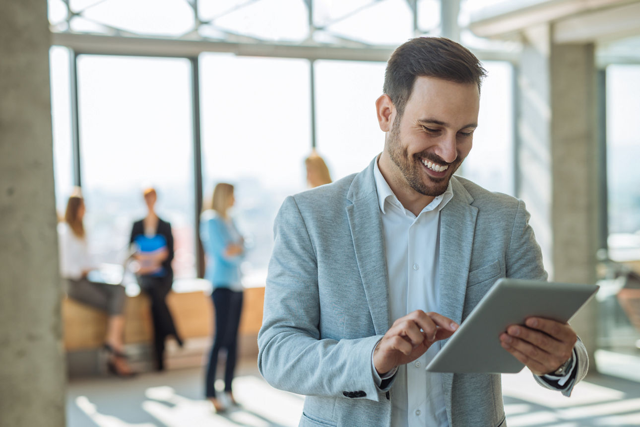 Mann im Anzug steht in einer Firma und schaut auf ein Tablet
