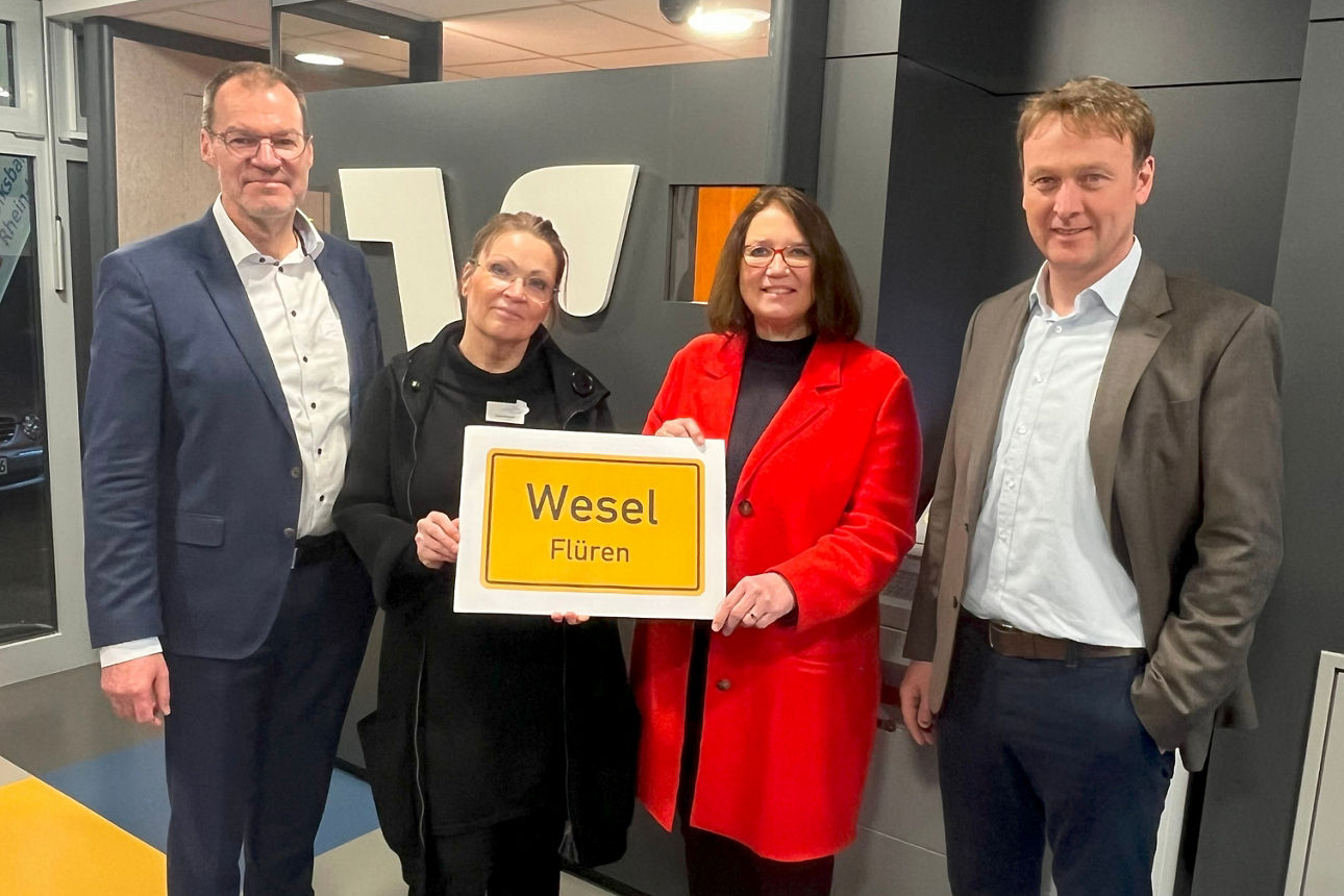 Eine Gruppe im Vorraum einer Filiale mit einem Schild auf dem "Wesel" steht.