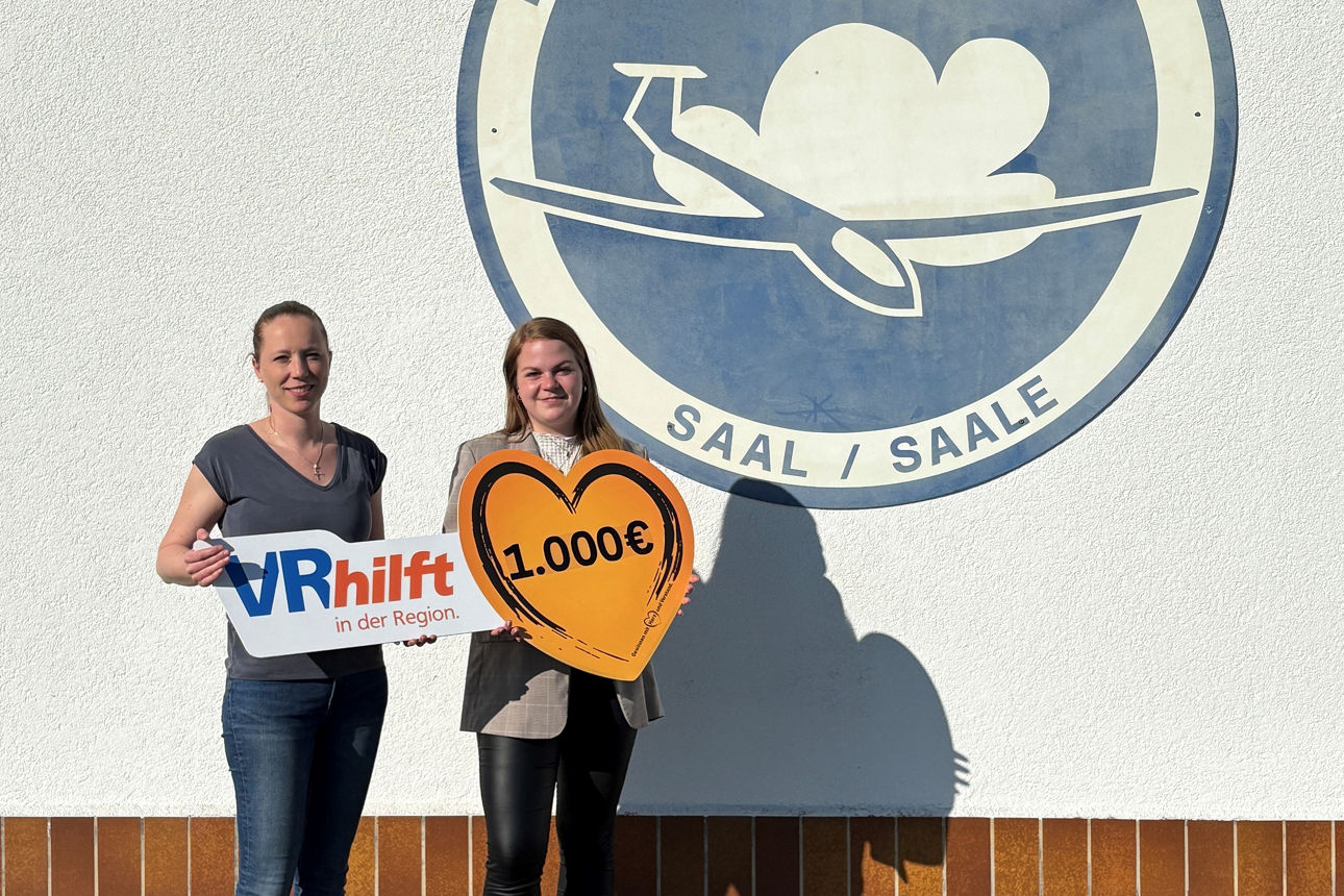 Das Bild zeigt zwei Frauen, die vor einer weißen Wand mit einem Logo stehen. Auf dem Logo steht: Flugsportverein Grabfeld. Si