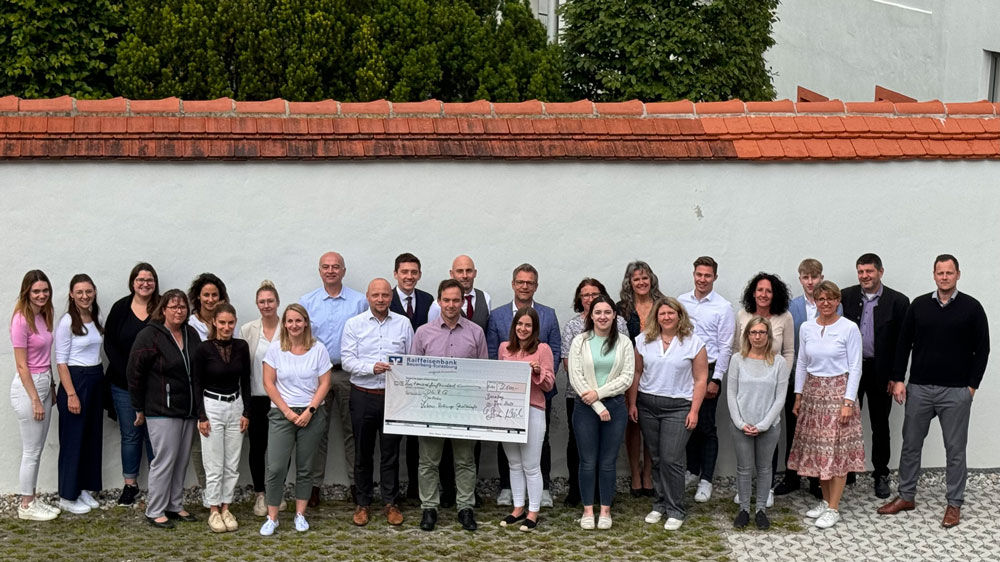 Mitglieder einer Organisation, die vor einer weiß gestrichenen Wand mit einer terrakottafarbenen Dachlinie stehen.