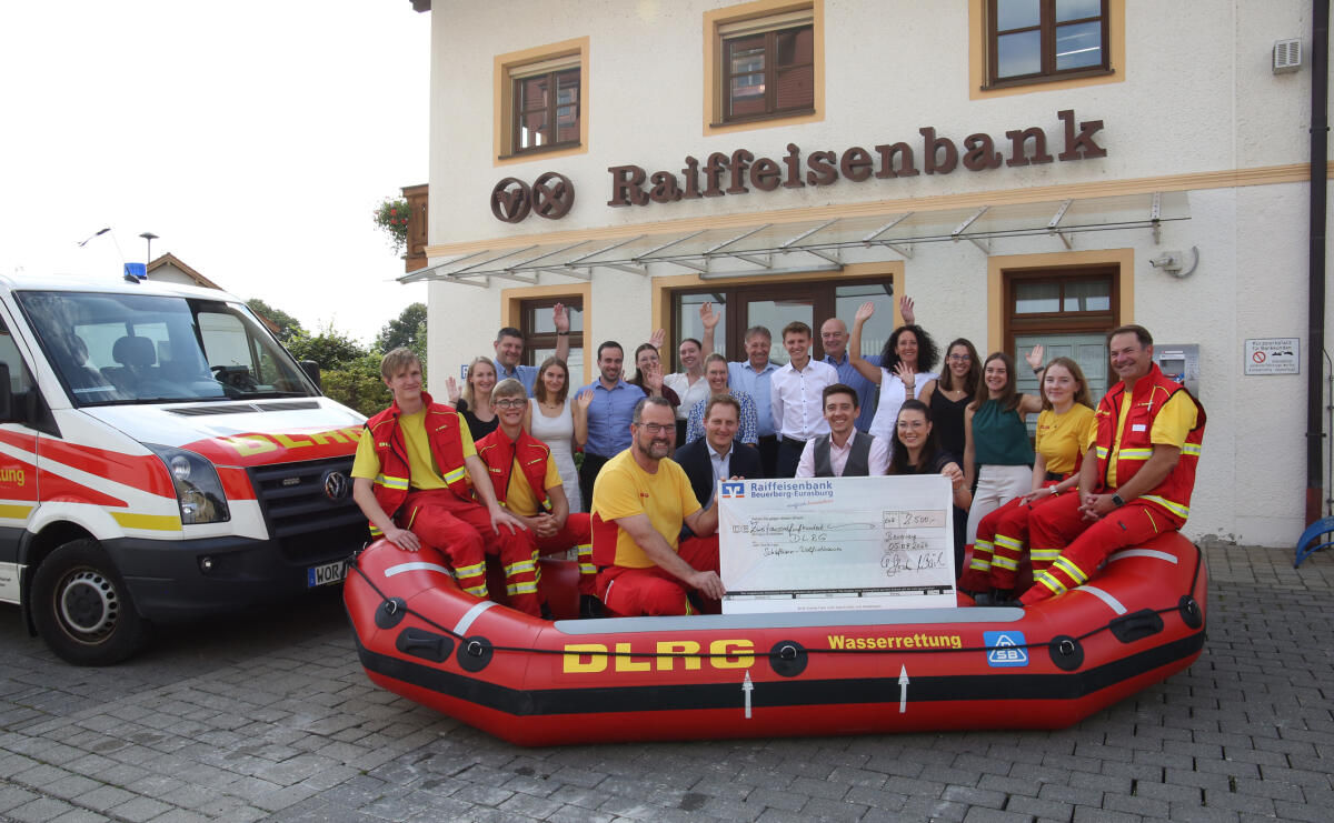 Gruppe von Menschen, darunter Mitglieder eines Wasserrettungsteams, stehen vor einer Raiffeisenbank 
