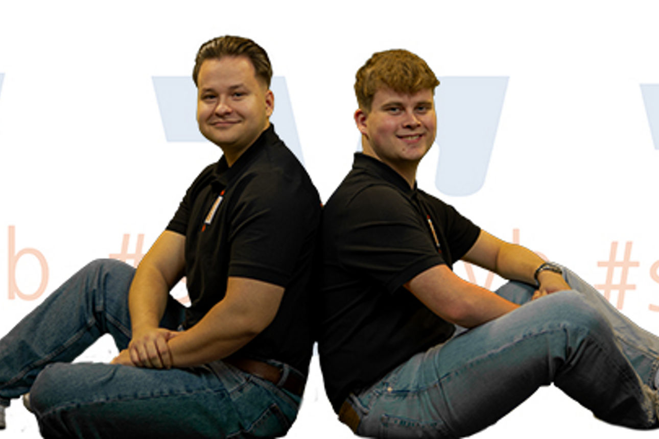 Zwei Personen, die in einer professionellen Umgebung Rücken an Rücken sitzen und nach vorne schauen.