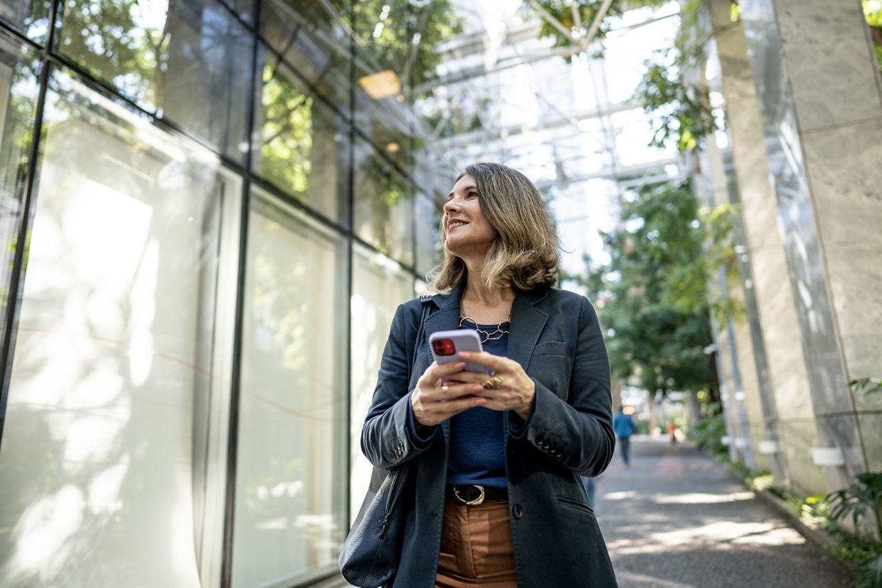 Eine Frau hält spazierend ihr Handy in der Hand