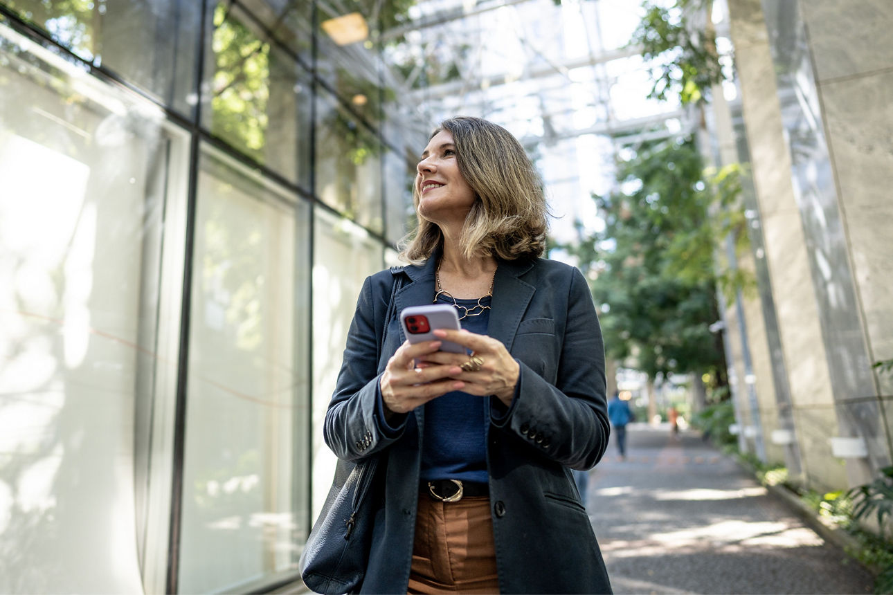 Eine Frau hält spazierend ihr Handy in der Hand