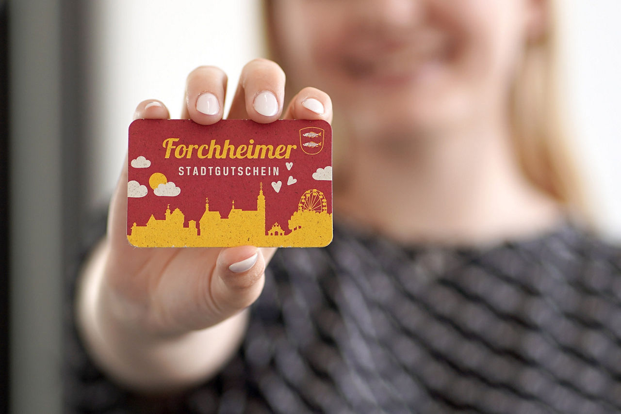 Frau hält mit der rechten Hand Forchheimer Stadtgutschein in die Kamera