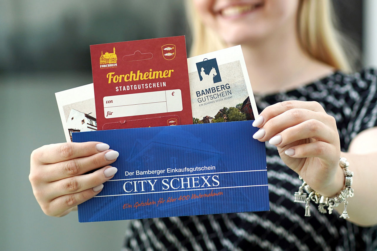Frau hält Bamberg Gutschein, CITY SCHEXS und Forchheimer Stadtgutschein in Händen