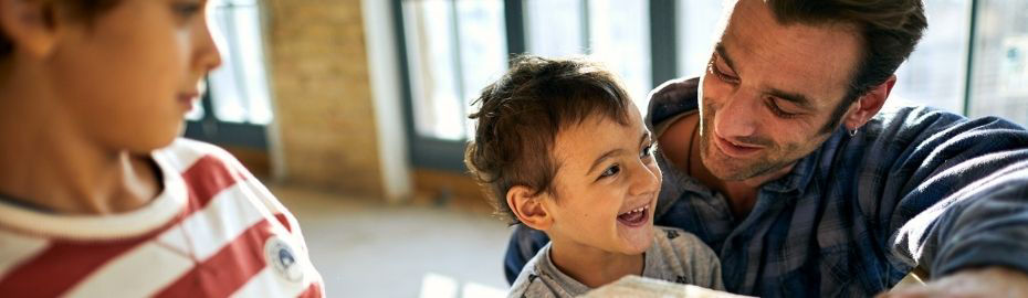 Ein Vater steht neben seinen zwei lachenden Kindern