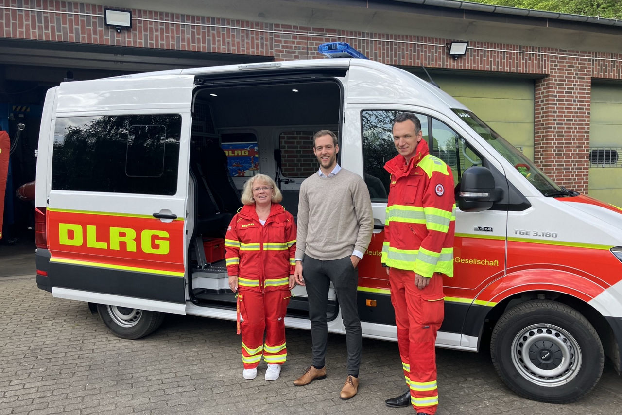 zwei Männer und eine Frau stehen von einem Rettungswagen der DLRG