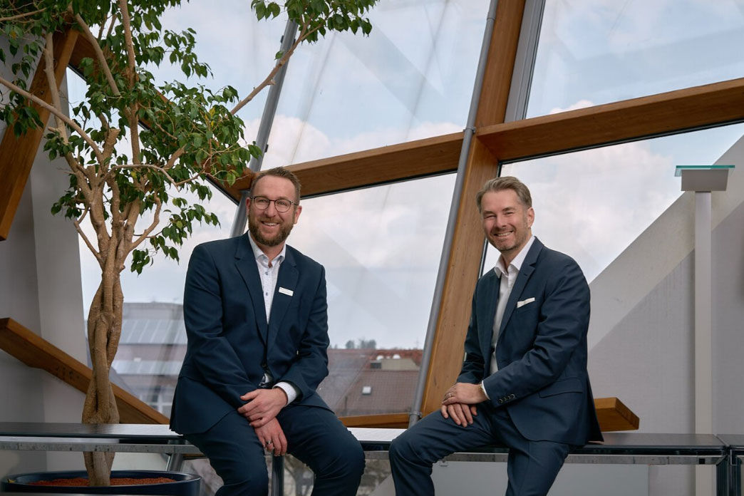 Vorstände der Bank sitzen vor großen Fenstern mit Ausblick.