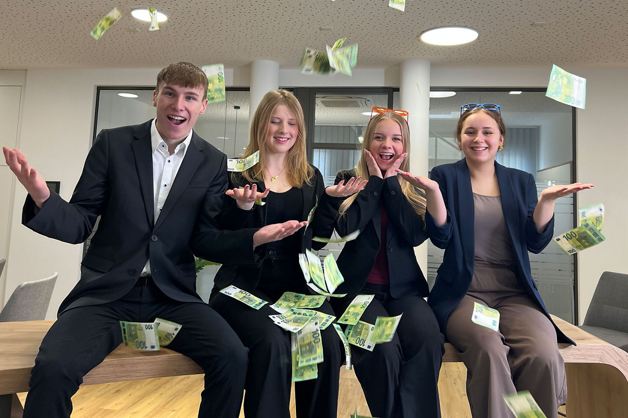 Unsere Azubis sitzen auf einem Tisch und werfen 100 Euro Scheine in die Luft und freue sich