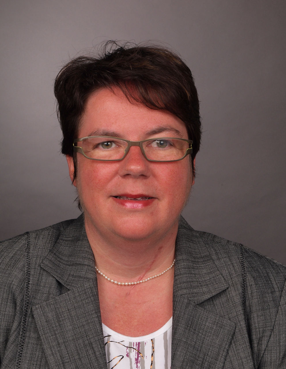 Mitarbeiterin der Bank in Business Kleidung und mit Brille lächelt in die Kamera.