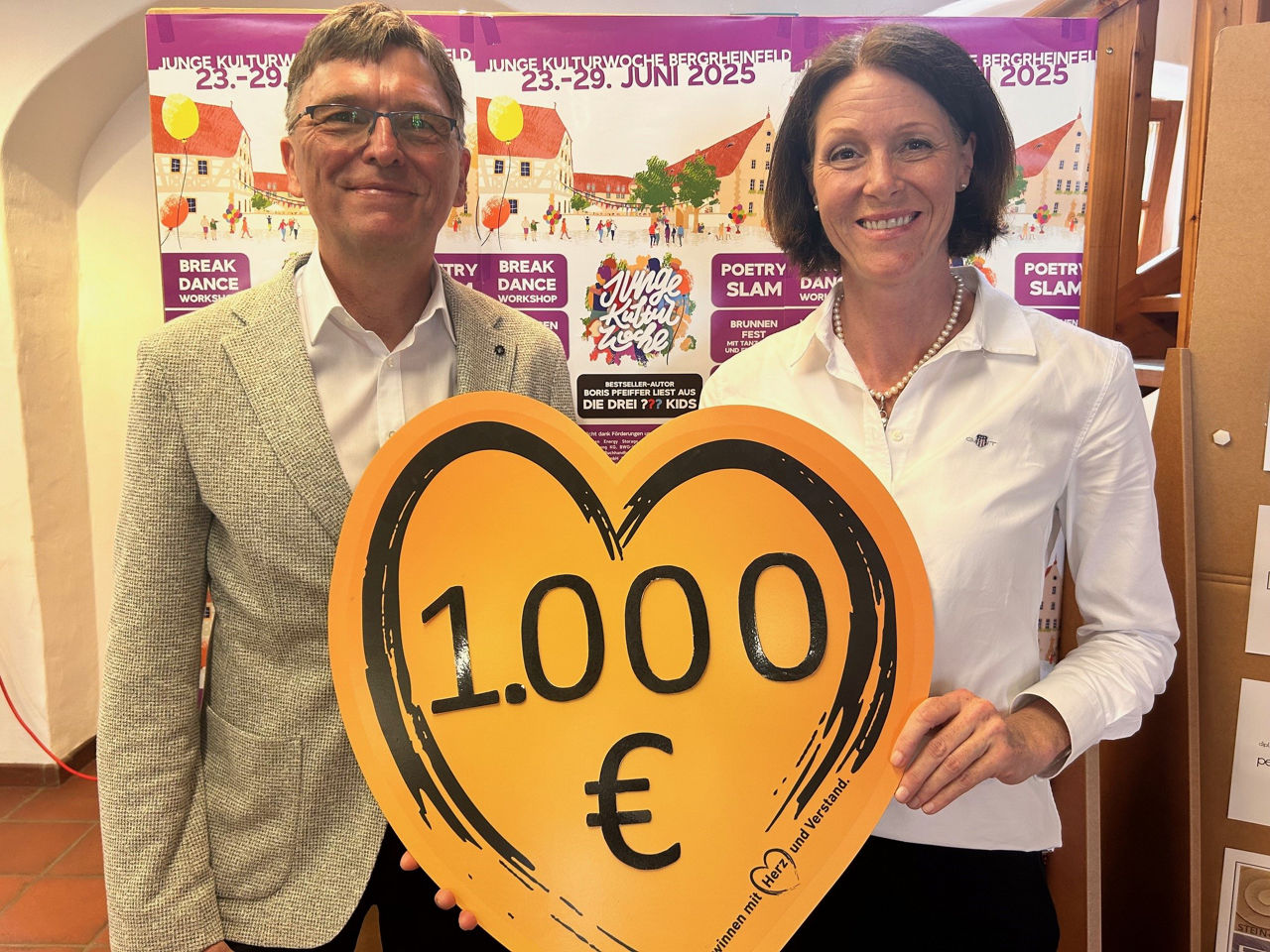 Frau und Mann halten lächelnd ein Herz mit Spendensumme 1.000 Euro