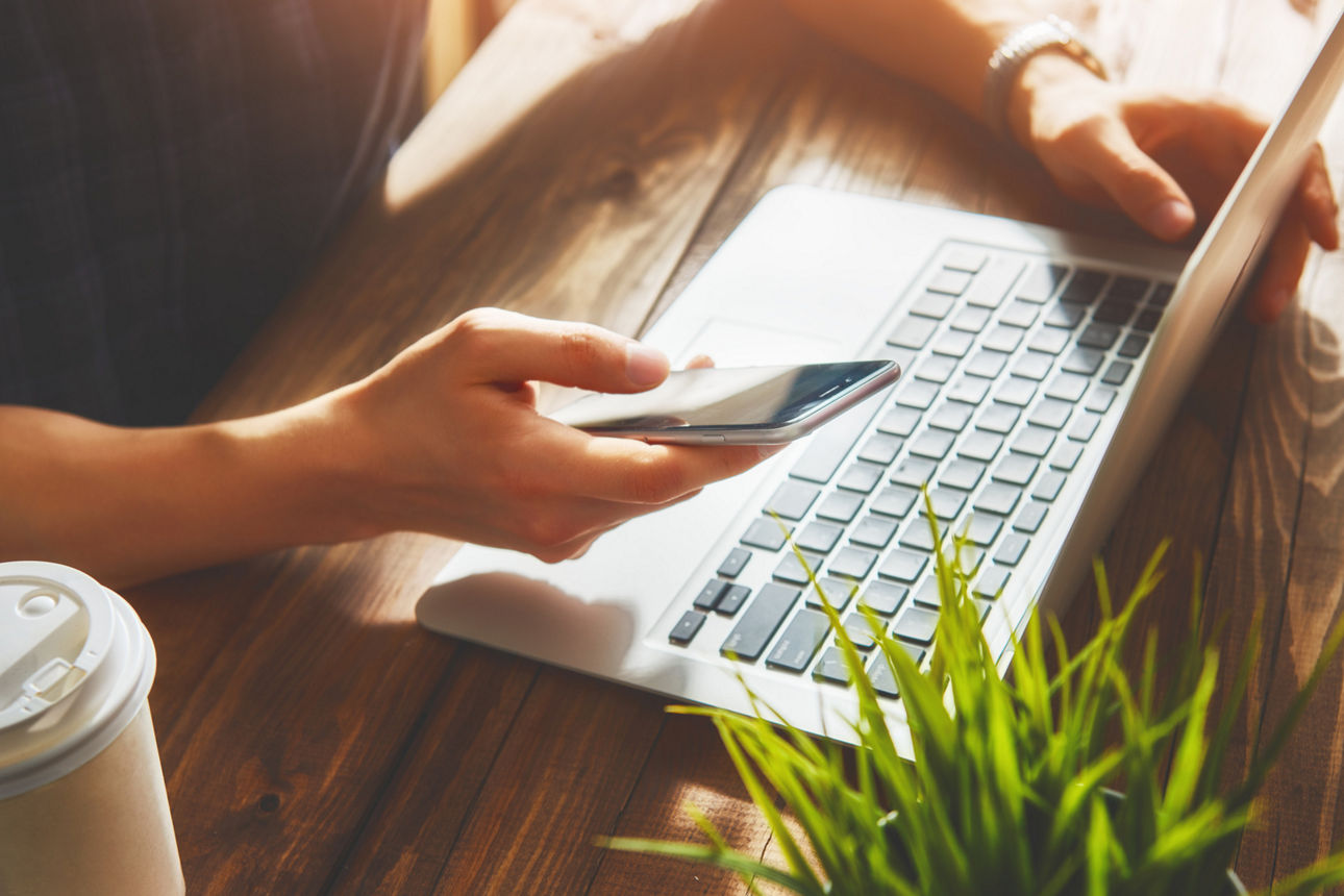 Person am Laptop mit Handy in der Hand