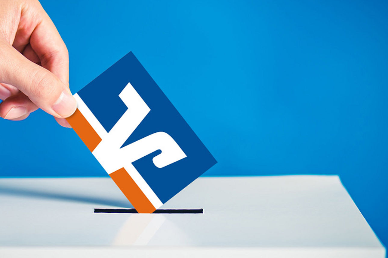Hand mit Stimmzettel über Wahlurne