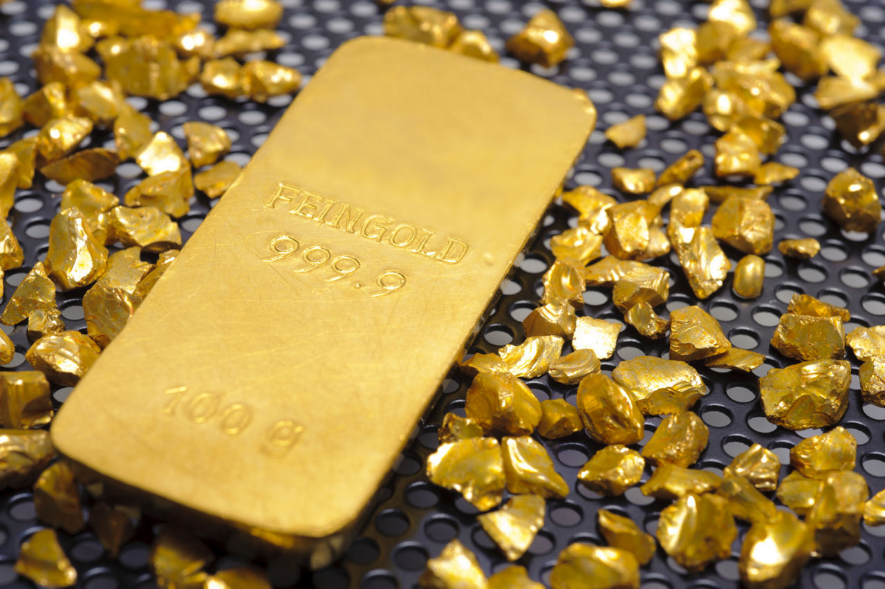 Goldbarren und Goldnauggets auf einem genoppten Untergrund.