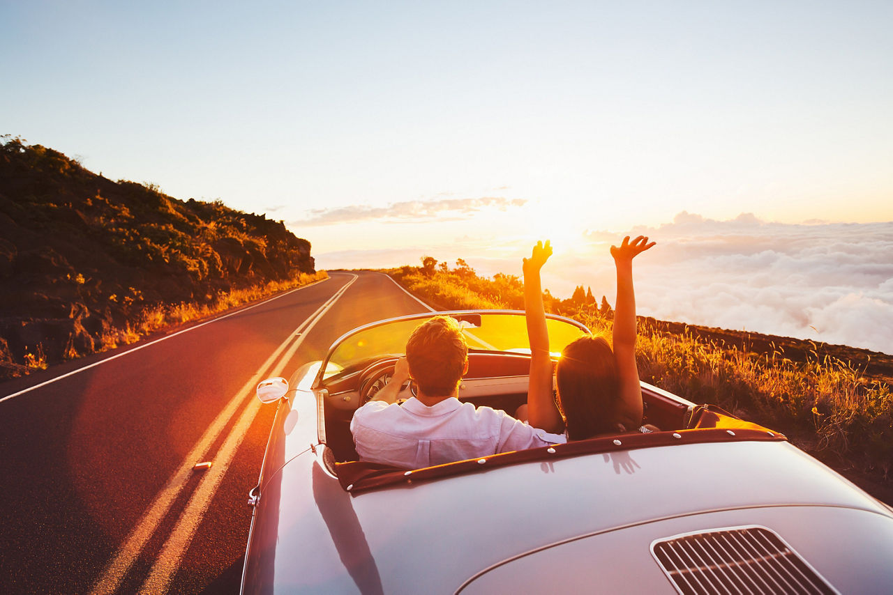 Paar fährt mit offenem Cabrio in den Sonnenuntergang