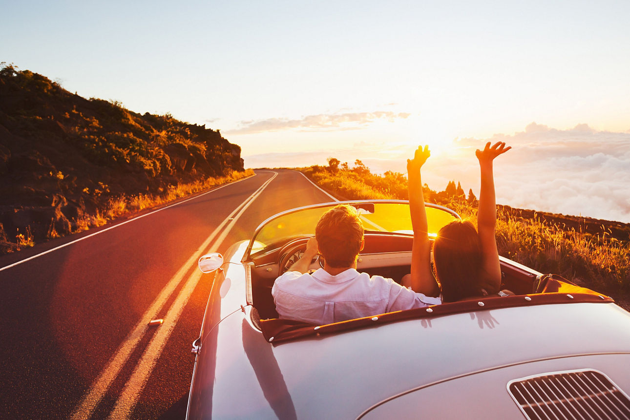 Paar fährt mit offenem Cabrio in den Sonnenuntergang