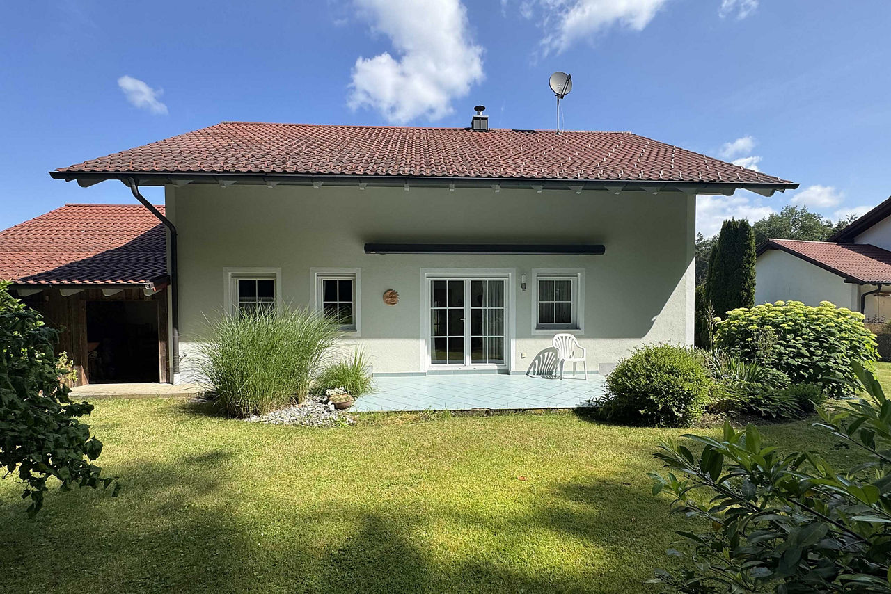 Ansicht eines Einfamilienhauses mit Terrasse und Garten. Das Haus hat eine helle Fassade, ein braunes Satteldach und große Fe
