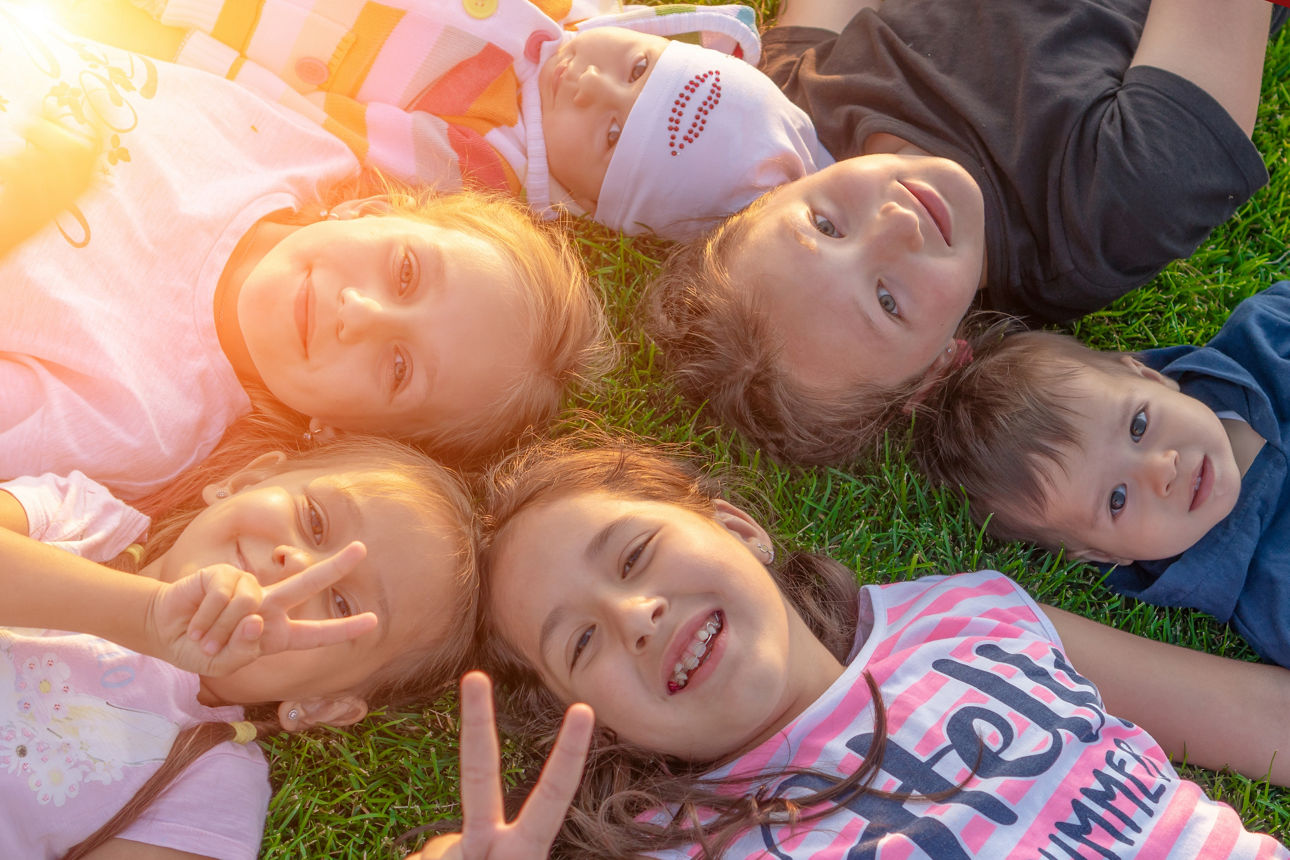 Eine Gruppe von Kindern liegt im Gras und lächelt hoch in die Kamera
