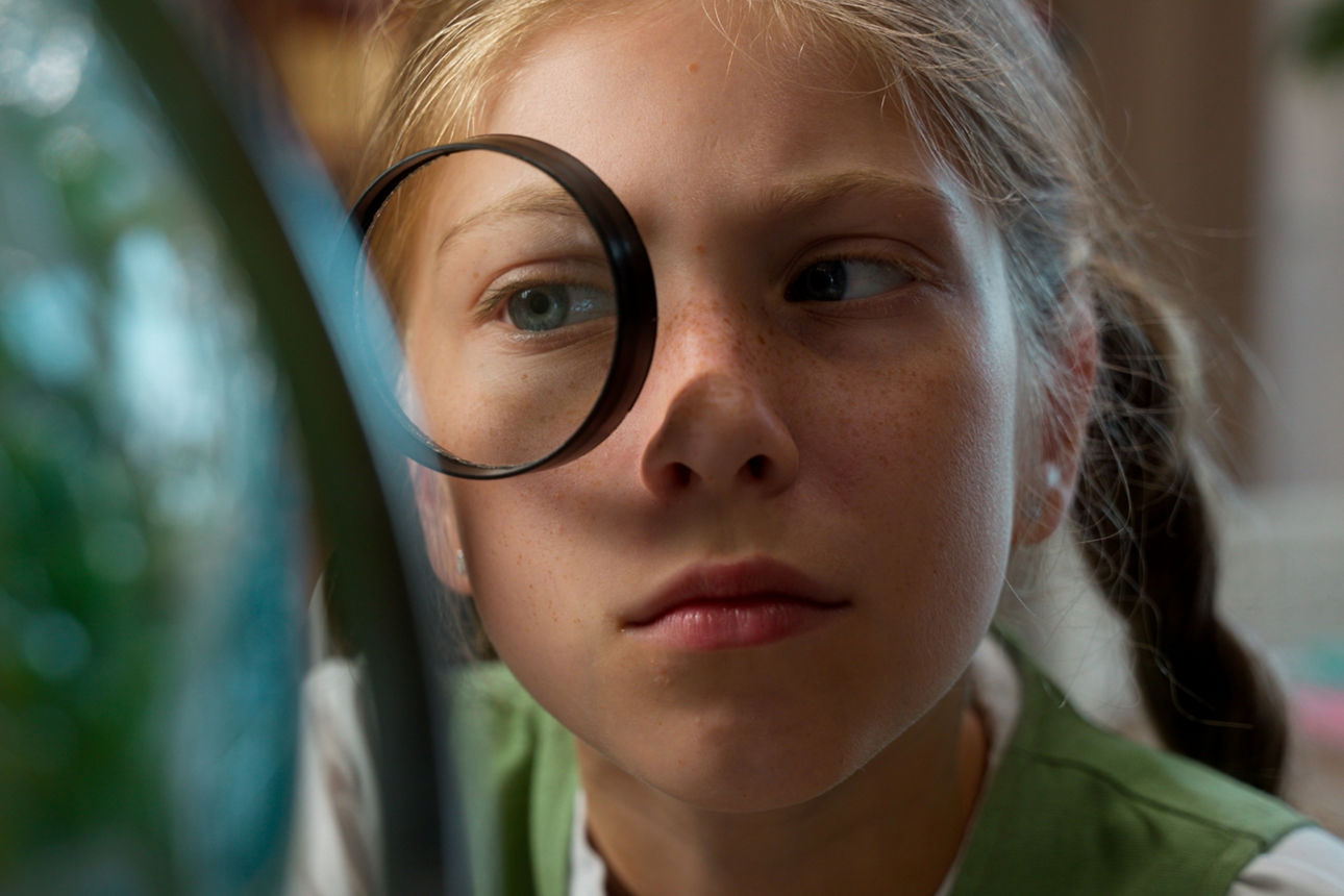 Ein Schulmädchen guckt sich einen Globus durch eine Lupe an.