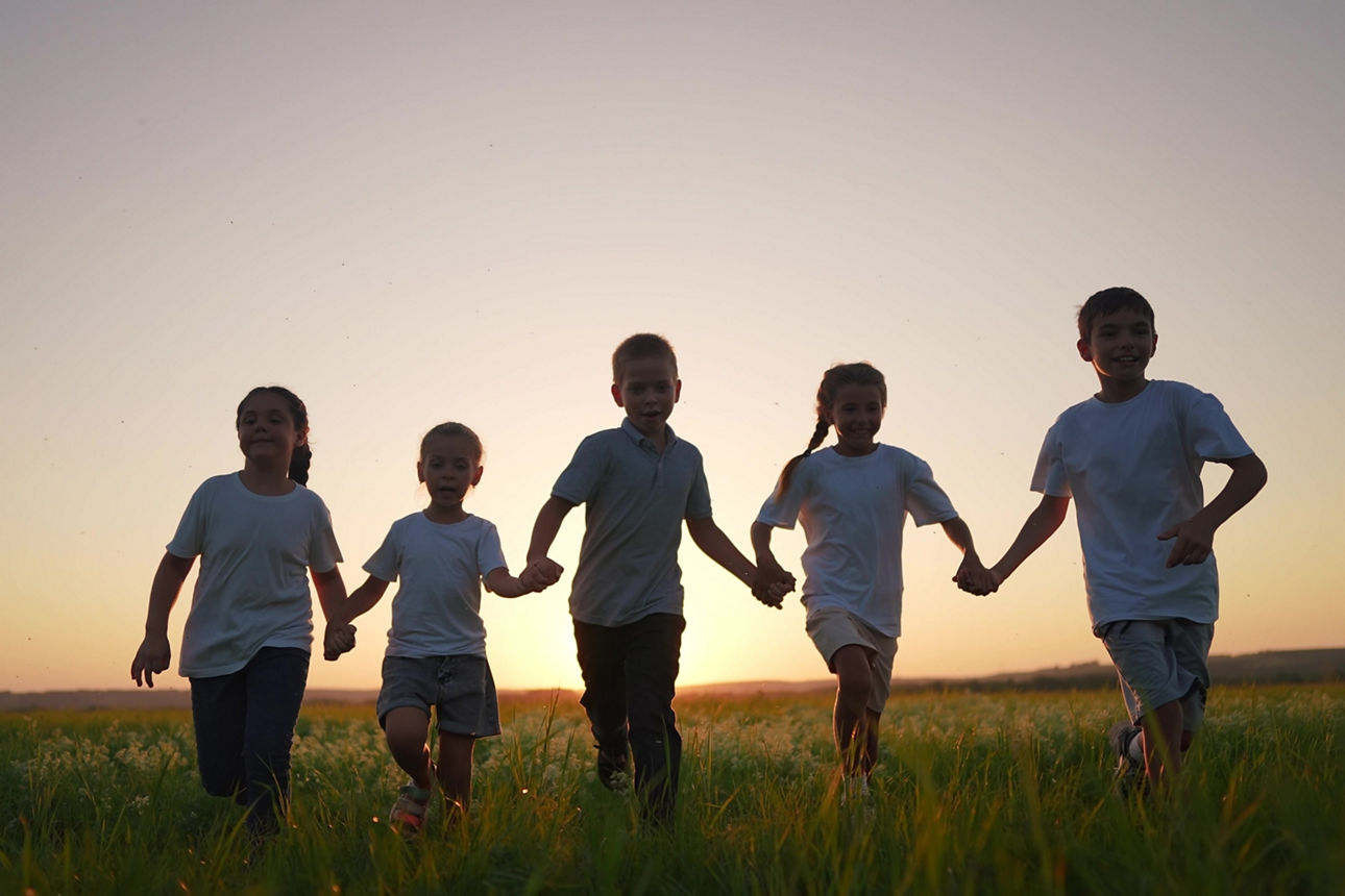 Eine Gruppe von Kindern hält sich an den Händen und läuft bei Sonnenuntergang über ein Feld.