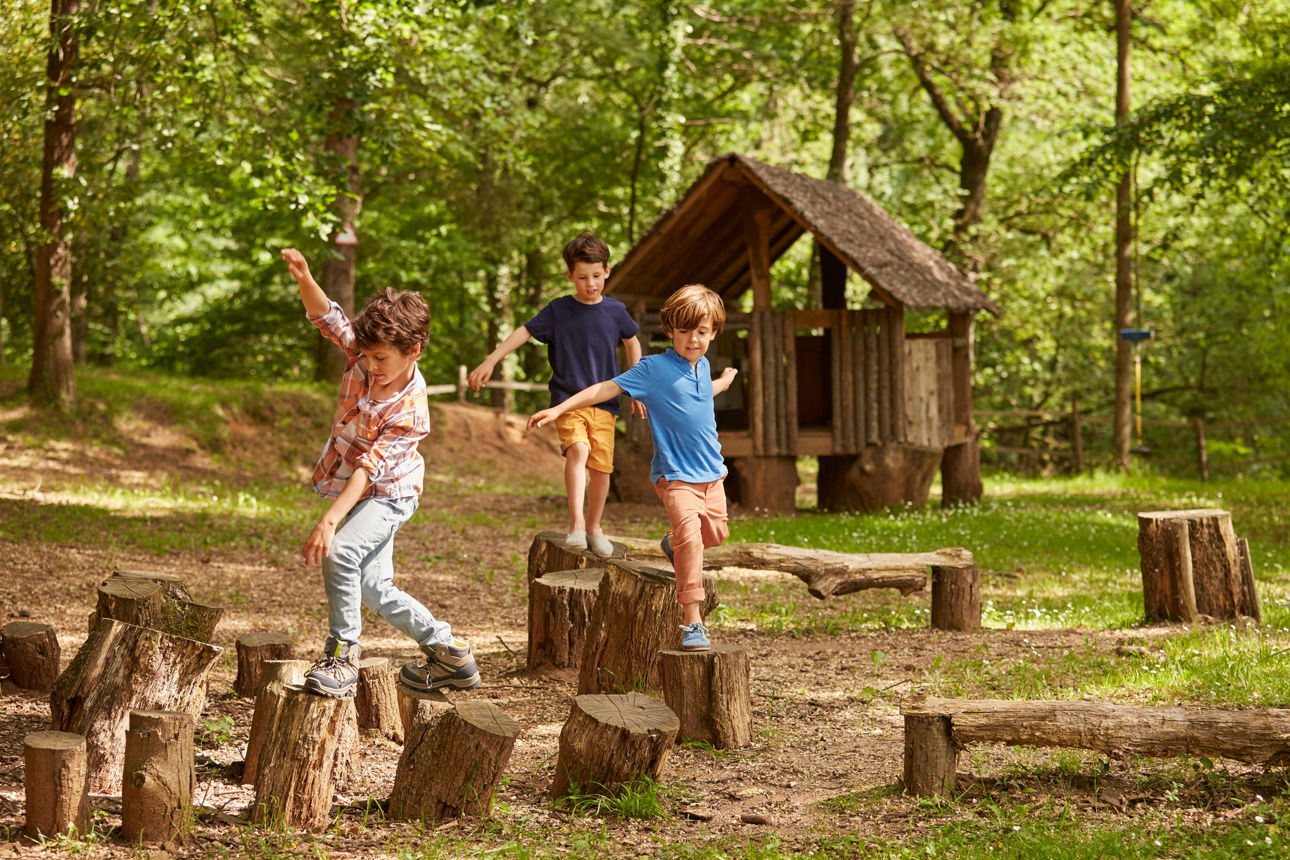 Drei Freunde spielen im Wald und hüpfen auf Baumstümpfe