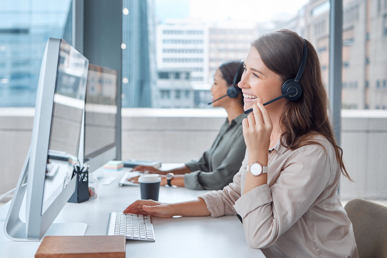 Zwei junge Frauen sitzen im Büro und telefonieren über ein Headset.