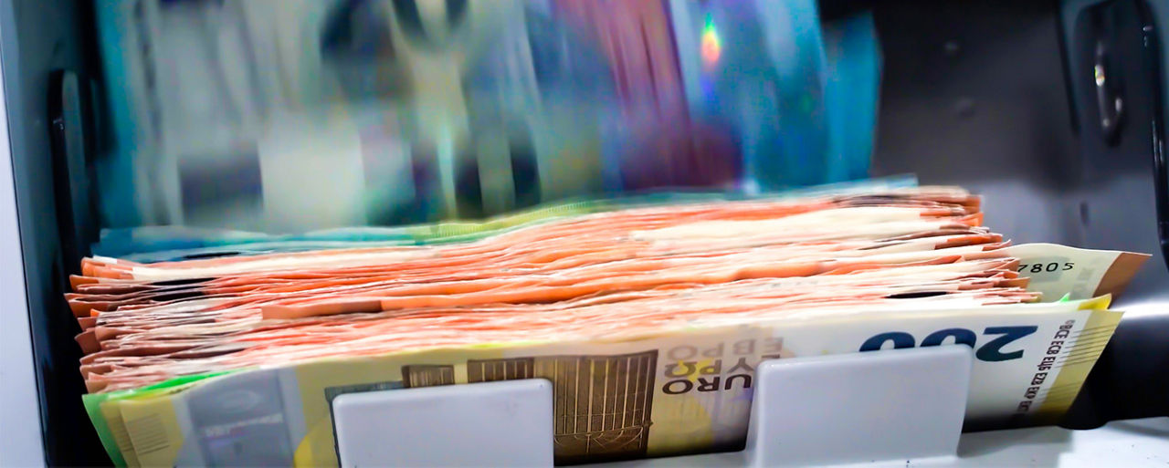 Nahaufnahme eines Geldautomats, der gerade Geld auszahlt. Es sind verschiedene Scheine zu erkennen.