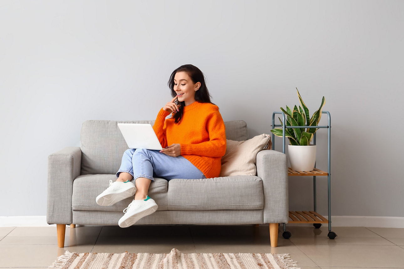 Frau sitzt mit aufgeklapptem Laptop auf einem Sofa 