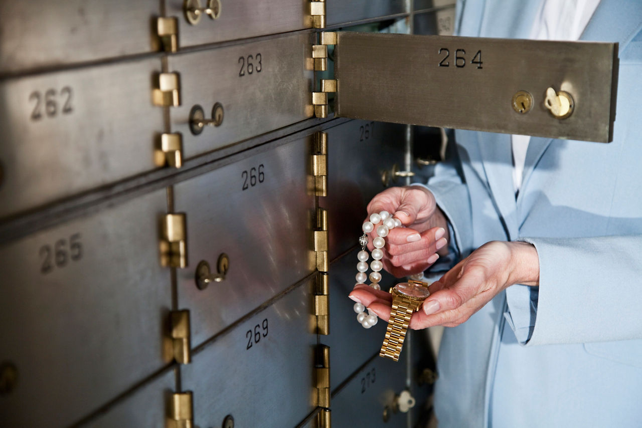 Frau vor offenem Bankschließfach mit Schmuck in der Hand