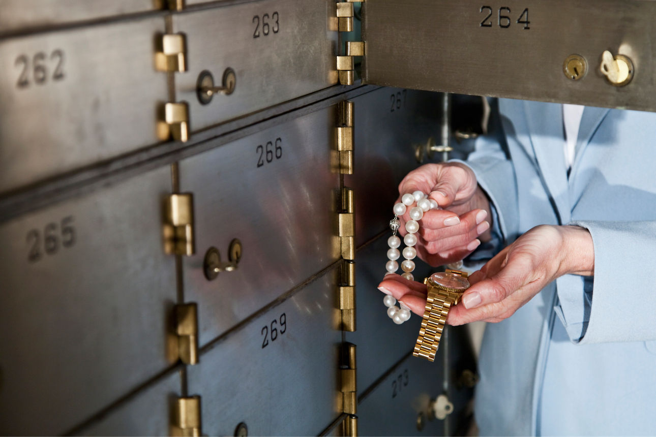 Frau vor offenem Bankschließfach mit Schmuck in der Hand