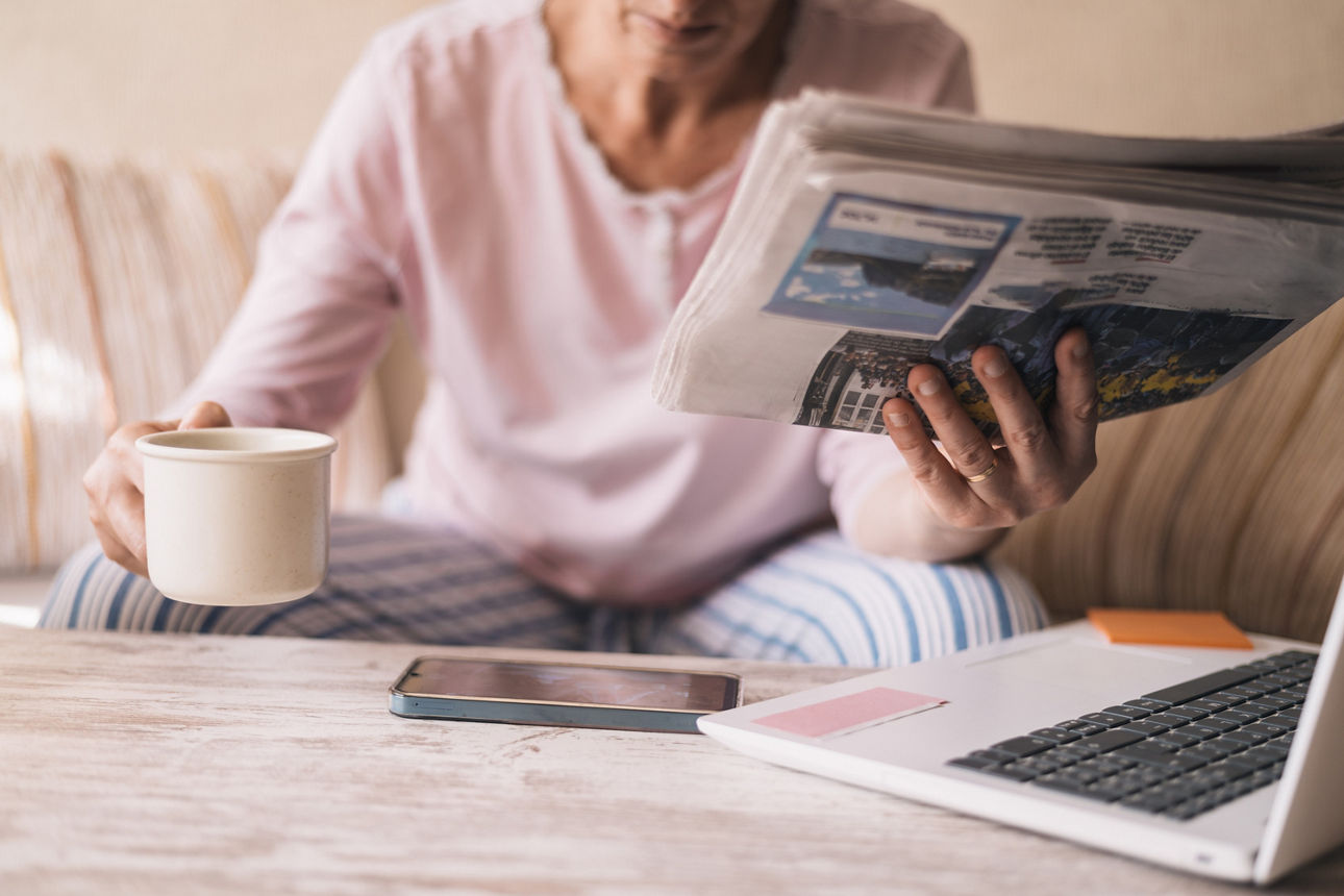 Frau auf dem Sofa mit einer Tasse Kaffee liest Zeitung.
